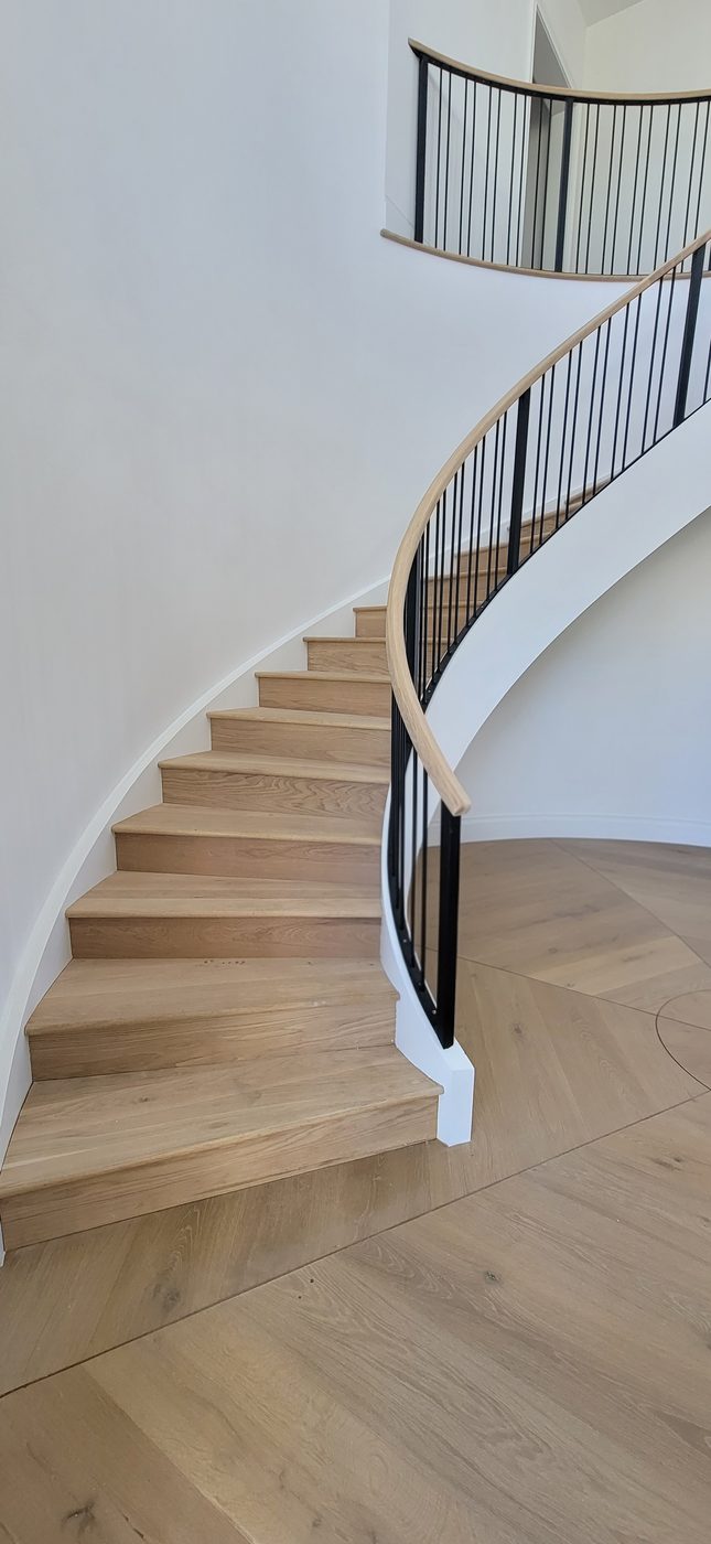 Curved wood staircase with black metal balusters