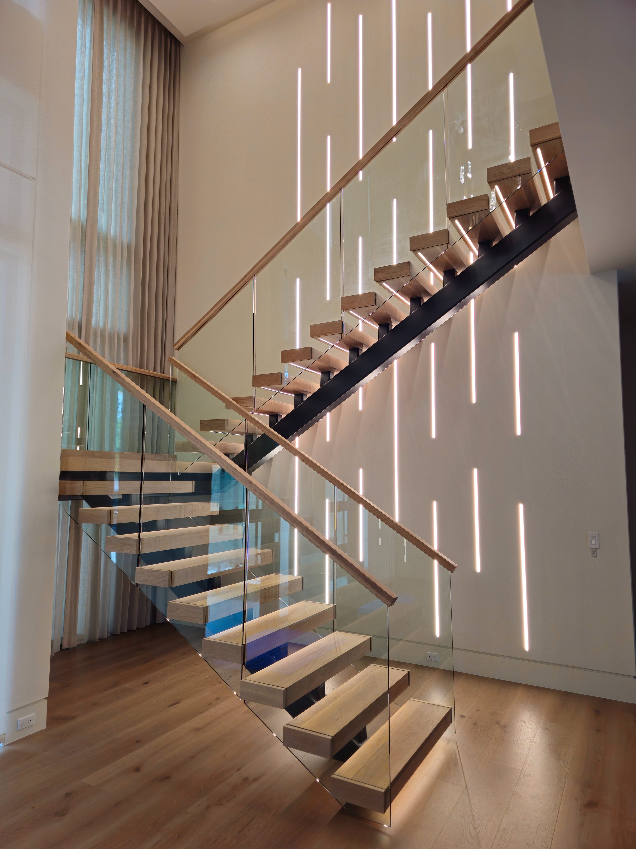 Floating wood staircase with glass railing and backlit feature wall